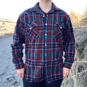 May include: A long-sleeved flannel shirt with a red, blue, and green plaid pattern. The shirt has a button-down front and two chest pockets.