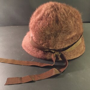 May include: A brown fuzzy hat with a wide brown ribbon tied in a bow at the front.