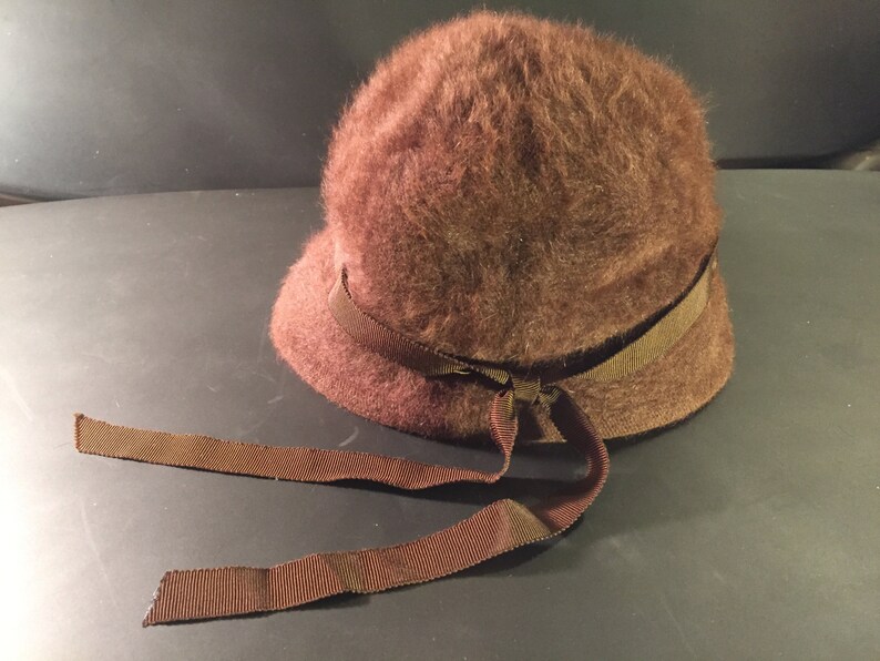 May include: A brown fuzzy hat with a wide brown ribbon tied in a bow at the front.