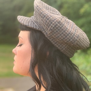May include: A person wearing a brown and black patterned newsboy cap. The cap has a flat top and a brim that curves down around the sides.