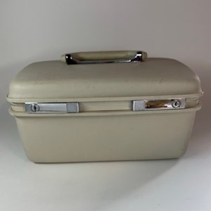 May include: A beige hard-sided travel case with a silver handle and latches.