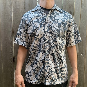 Può includere: Una camicia a maniche corte con bottoni e stampa di ananas e foglie in bianco e nero.