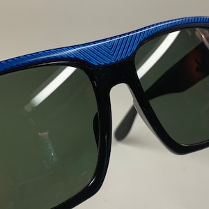 Peut inclure: Lunettes de soleil noires avec des montures &agrave; motifs bleus et blancs. Les verres sont vert fonc&eacute;.