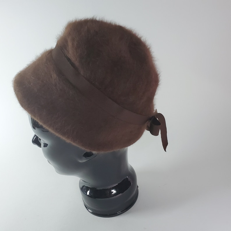 May include: A brown fuzzy bucket hat with a brown satin ribbon tied in a bow at the back.
