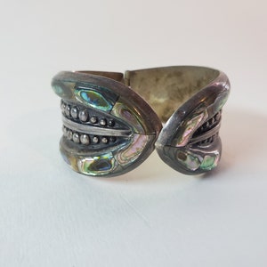 May include: A silver bracelet with a hinged design, featuring abalone shell inlay and a beaded detail.