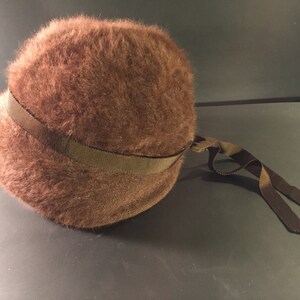 May include: A brown fuzzy hat with a brown ribbon tied around it.