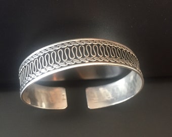 May include: Silver bracelet with a detailed, intricate design of interwoven loops around the band.