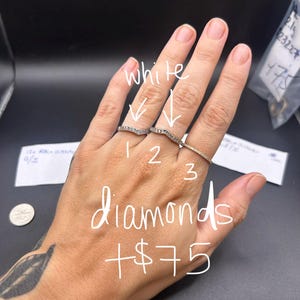 May include: Three silver-toned chevron-shaped rings featuring small embedded stones, labeled with the numbers 1, 2, and 3. The image includes handwritten text that reads white, diamonds, and +$75, along with a small circular coin for scale.
