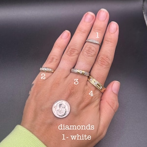 May include: Four rings labeled 1 through 4 are displayed on fingers. Ring 1 is a thin silver band, ring 2 is a gold band with stones, ring 3 is a gold band with stones, and ring 4 is a wider gold band with stones. A US dime is present for scale.