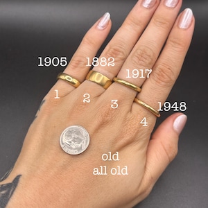 May include: Four gold bands labeled 1, 2, 3, and 4 with corresponding years 1905, 1882, 1917, and 1948. A silver dime is positioned near the rings for scale. The text 'old all old' is visible below the coin. The bands vary in width and thickness.