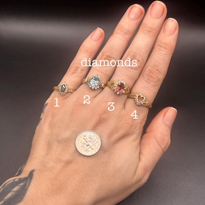 May include: Four gold rings with gemstones are displayed, labeled 1 through 4. The rings feature various stone shapes and colors, including a dark green, light blue, and red stone. The word "diamonds" is written above the rings.