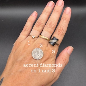 May include: Three gold rings worn on fingers. Ring 1 features a small diamond, ring 2 is a plain gold band, and ring 3 is a rectangular black onyx ring with a diagonal row of accent diamonds. A US dime coin is placed for scale.