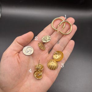 May include: A collection of four gold-toned earring styles labeled with numbers one through four. Item one is a pair of hoop earrings, two are oval textured studs, three are domed studs with striped patterns, and four are knotted circular studs.