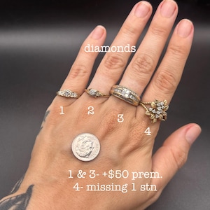 May include: Four gold-toned rings labeled 1 through 4, featuring various diamond settings. Ring 1 and 2 are thin bands with small stones. Ring 3 is a wide band with baguette and round diamonds. Ring 4 has a floral design with multiple stones.