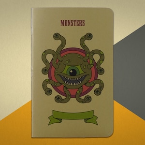 May include: A brown notebook with the word "MONSTERS" printed on the front cover. The cover features a green, multi-eyed monster with a toothy grin and a red and purple circle behind it.