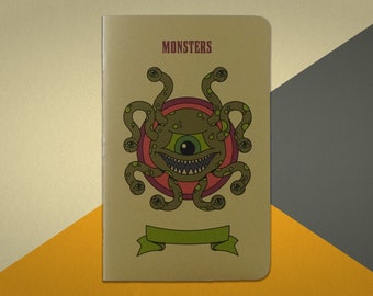 May include: A brown notebook with the word "MONSTERS" printed on the front cover. The cover features a green, multi-eyed monster with a toothy grin and a red and purple circle behind it.