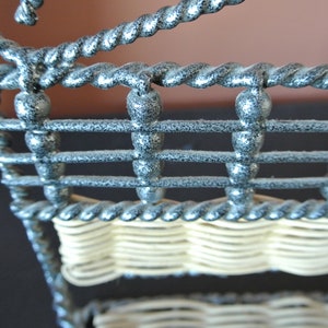 Pu&ograve; includere: Primo piano di una rastrelliera in filo metallico argentato con un fondo in vimini intrecciato. La rastrelliera ha un design a corda decorativo ed &egrave; realizzata in filo ritorto.