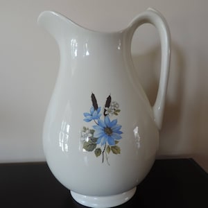 May include: White ceramic jug with a blue and white floral design. The jug has a wide base and a handle.