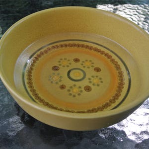 Puede incluir: Un taz&oacute;n de cer&aacute;mica amarillo con un patr&oacute;n geom&eacute;trico marr&oacute;n y blanco. El taz&oacute;n est&aacute; lleno de agua.