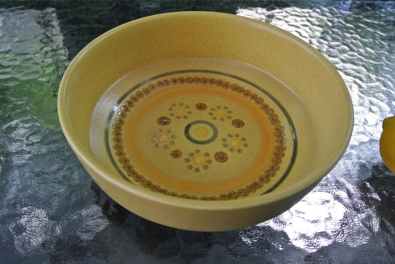 Puede incluir: Un taz&oacute;n de cer&aacute;mica amarillo con un patr&oacute;n geom&eacute;trico marr&oacute;n y blanco. El taz&oacute;n est&aacute; lleno de agua.