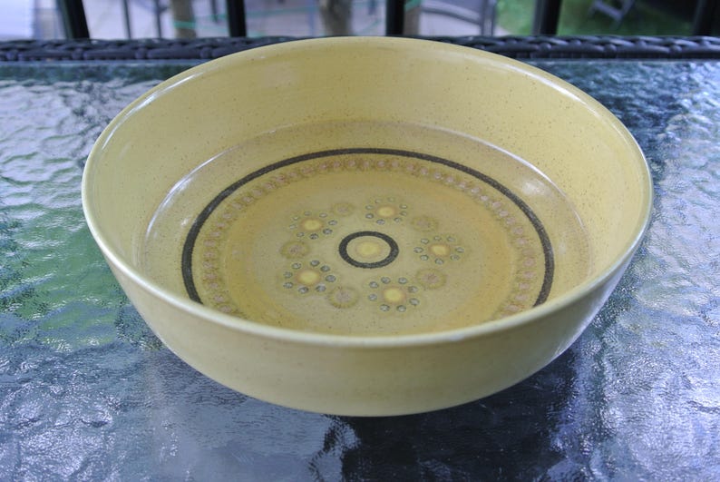 Puede incluir: Un taz&oacute;n grande de cer&aacute;mica amarilla con un dise&ntilde;o geom&eacute;trico marr&oacute;n y blanco. El taz&oacute;n est&aacute; vac&iacute;o y est&aacute; sobre una mesa de vidrio.