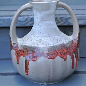 May include: A ceramic vase with two handles, featuring a white glaze with brown and red accents. The vase has a drip glaze effect, creating a unique and rustic look.