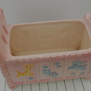 Könnte beinhalten: Ein rosa Keramik-Babybett-Pflanztopf mit einem weißen und blauen Giraffen-, einem blauen und weißen Schuh- und einem blauen und weißen Vogeldesign.