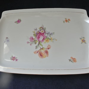 May include: A white rectangular serving tray with a gold trim and a floral design featuring pink, yellow, and orange flowers.