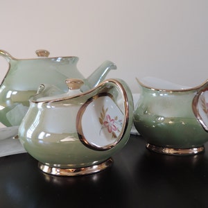 Peut inclure: Un service à thé vert avec une théière, un pot à crème et un sucrier. L'ensemble est décoré de motifs floraux et de bordures dorées.