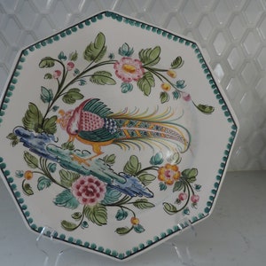 May include: Octagonal ceramic plate with a white background and a hand-painted design of a colorful bird with a long tail, surrounded by green leaves and pink and yellow flowers.