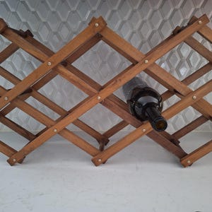 Peut inclure: Un porte-bouteilles en bois avec un design en croisillon, tenant une seule bouteille de vin. Le porte-bouteilles est en bois brun clair et a un aspect rustique.