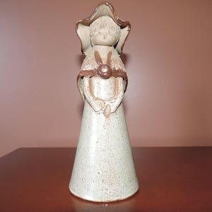 May include: A ceramic figurine of a woman wearing a brown hat and dress. The figurine is painted in shades of brown and white.