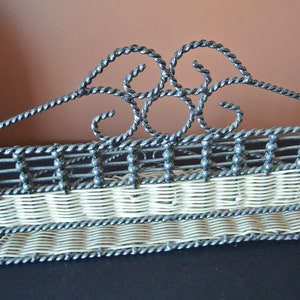 Pu&ograve; includere: Un ripiano in metallo nero con un design in vimini bianco. Il ripiano ha due livelli e un design decorativo a volute nella parte superiore.