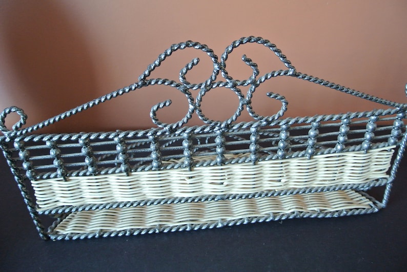 Pu&ograve; includere: Un ripiano in metallo nero con un design in vimini bianco. Il ripiano ha due livelli e un design decorativo a volute nella parte superiore.