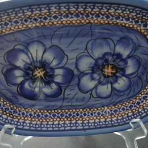 May include: An oval blue ceramic serving dish with a white and brown border. The dish features two blue flowers with brown centers.