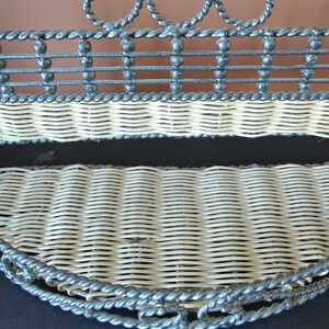 Pu&ograve; includere: Un ripiano a muro in metallo grigio con due ripiani in vimini intrecciato. Il ripiano ha un design decorativo a corda attorno ai bordi.