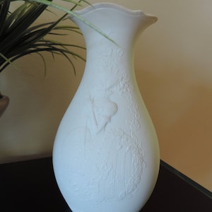 May include: White ceramic vase with an embossed floral design. The vase has a wide mouth and a narrow base.