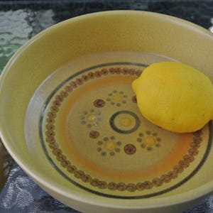 Puede incluir: Un lim&oacute;n amarillo en un taz&oacute;n de cer&aacute;mica marr&oacute;n y amarillo con un patr&oacute;n decorativo.