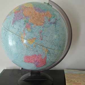 Może przedstawiać: Niebieski globus na czarnym stojaku, przedstawiający mapę świata z kontynentami w różnych kolorach. Globus jest przechylony, aby pokazać Azję i Australię.