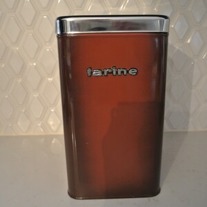 Peut inclure: Une boîte en métal marron avec un couvercle argenté et le mot "farine" imprimé sur le devant.