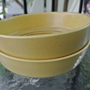 Puede incluir: Dos cuencos de cer&aacute;mica amarilla apilados uno encima del otro. Los cuencos tienen una textura moteada y una forma ligeramente redondeada.