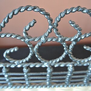 Pu&ograve; includere: Primo piano di una recinzione metallica decorativa con un design a corda intrecciata. La recinzione &egrave; dipinta in argento con una lavata nera.