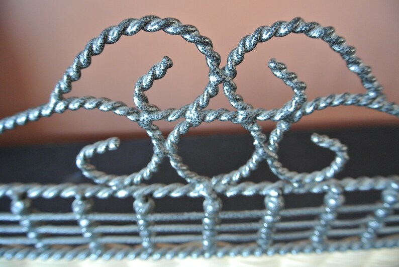 Pu&ograve; includere: Primo piano di una recinzione metallica decorativa con un design a corda intrecciata. La recinzione &egrave; dipinta in argento con una lavata nera.