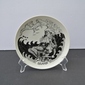 Puede incluir: Un plato de cerámica blanco con una ilustración en blanco y negro de un hombre barbudo sentado en una ola. El plato tiene la palabra "ISLAND" escrita en la parte inferior.