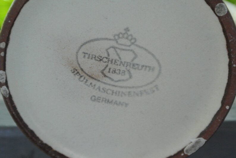 Pode incluir: Close-up de uma caneca de cer&acirc;mica branca com uma borda marrom. A caneca tem um logotipo marrom que diz "Tirschenreuth 1832 Spulmaschinenfest Germany".