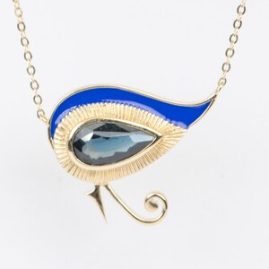 May include: A gold necklace with a blue and gold pendant shaped like a stylised bird. The pendant features a dark blue gemstone.