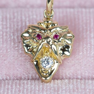 May include: Close-up of a gold dragon pendant featuring ruby eyes and a central diamond. The dragon's mouth is open, revealing the diamond. The pendant is intricately detailed and has a three-dimensional quality.  The gold is a bright, shiny yellow, and the rubies are a deep, rich red. The diamond is clear and sparkly. The pendant is shown against a pink velvet background.