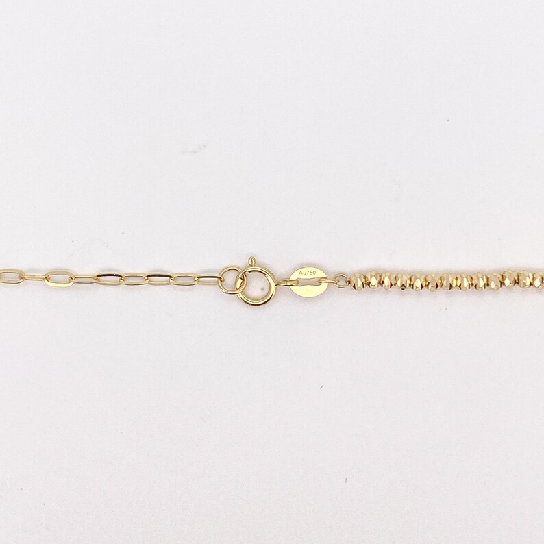Puede incluir: Primer plano de un collar de oro con una cadena delicada y una secci&oacute;n con cuentas texturizadas. El collar presenta un cierre de mosquet&oacute;n y una peque&ntilde;a etiqueta con la marca A.750.