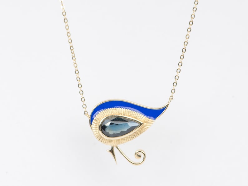 May include: A gold necklace with a blue and gold pendant shaped like a stylised bird. The pendant features a dark blue gemstone.