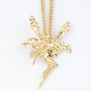 Peut inclure: Un collier pendentif doré représentant une fée. La fée a des ailes déployées et est suspendue à une chaîne dorée assortie. Le pendentif est orné de motifs complexes et se détache sur un fond blanc.